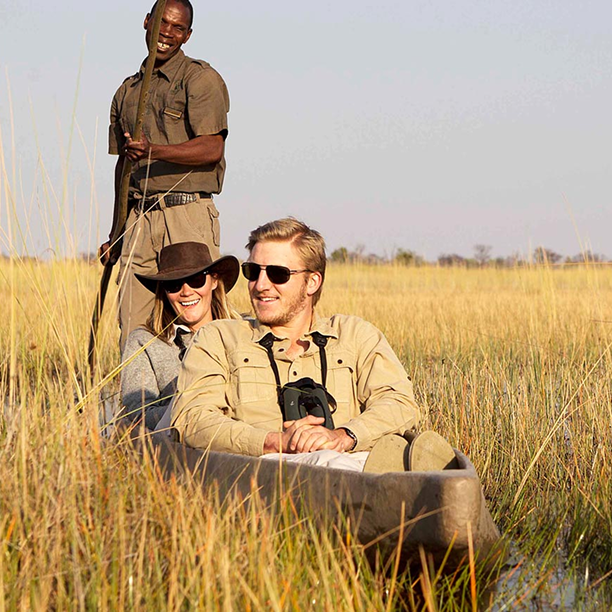 Safari guide and two tourists traveling by mokoro canoe through tall grass in Botswana’s Okavango Delta.