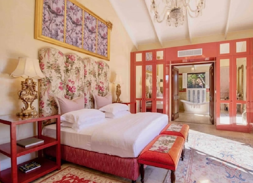 Elegant luxury bedroom with a floral upholstered bed, red accents, ornate furnishings, and a chandelier.