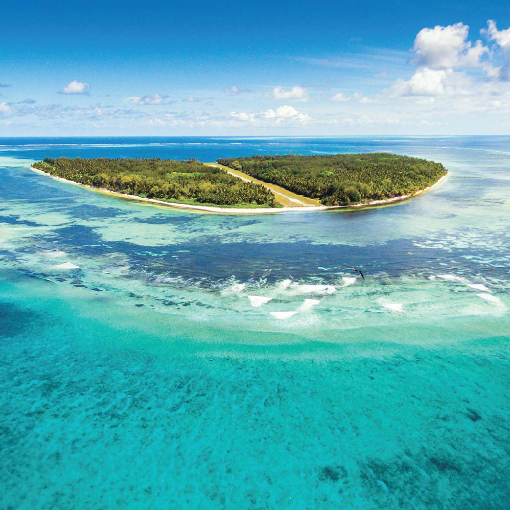 Tropical island lagoon with crystal-clear turquoise water, lush green hills, and a bright blue sky with clouds.