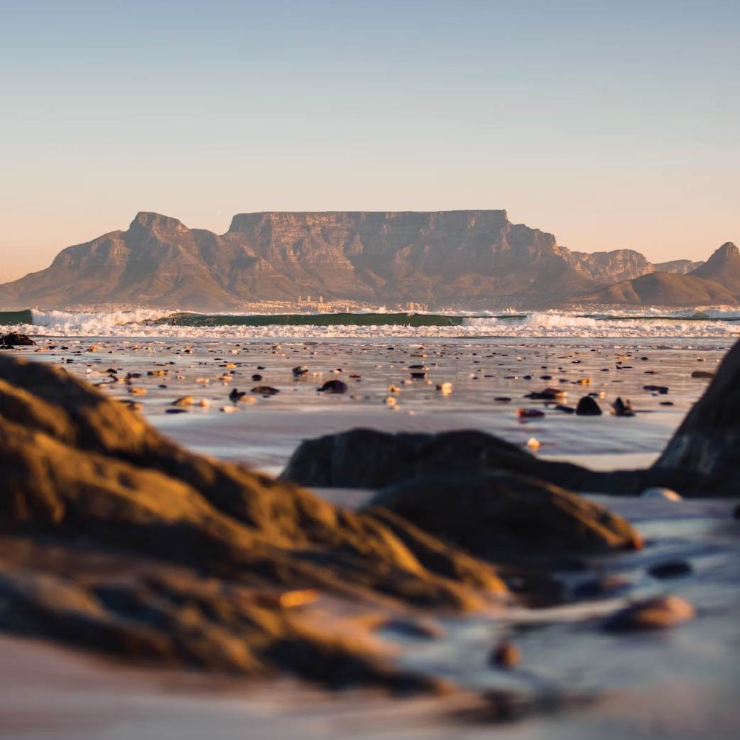 View of Table Mountain overlooking the rocky shoreline and calm waters near Cape Town, South Africa.