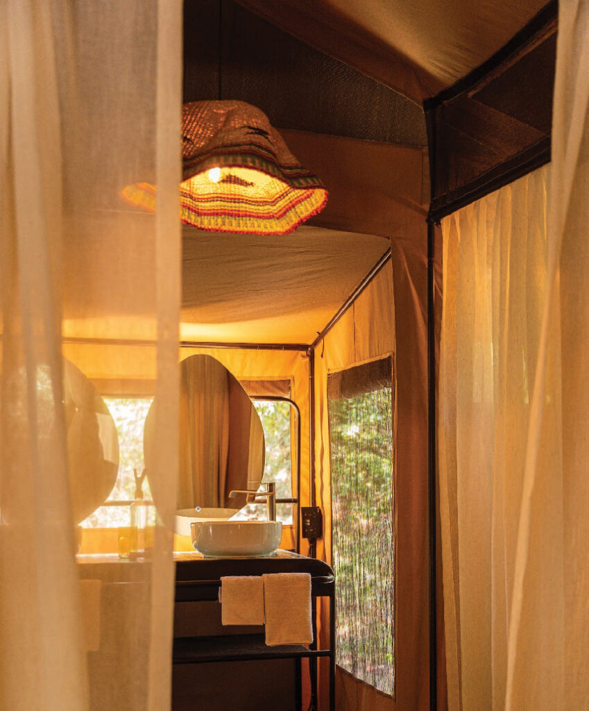 En-suite tented bathroom at Kenya Bush Camp, featuring a vanity sink, round mirror, warm lighting, and canvas walls.