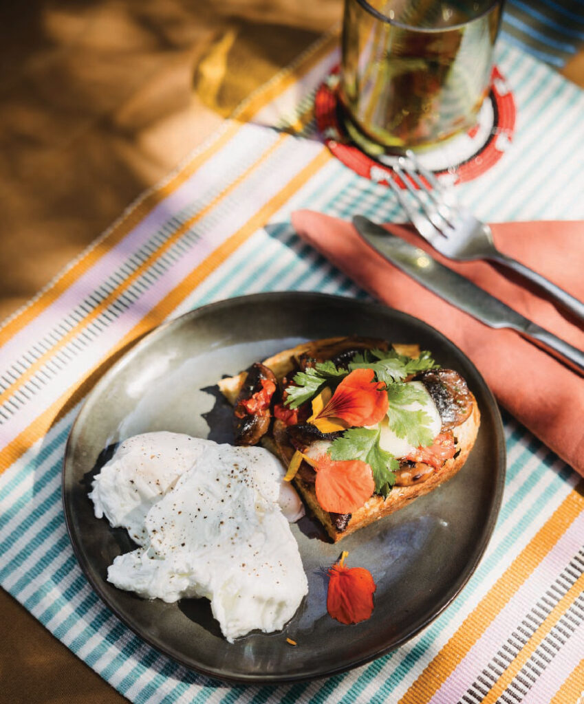 Safari breakfast featuring avocado toast topped with herbs and edible flowers, served with poached eggs on a plate.