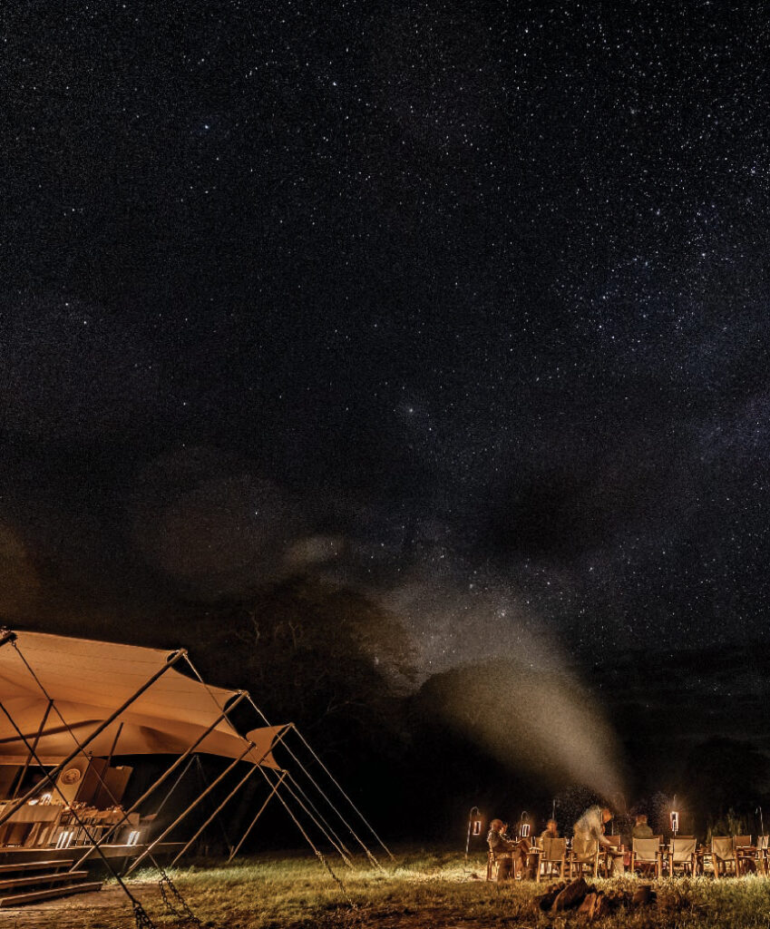 Luxury safari tents beside a campfire under a star-filled night sky in Gorongosa, Mozambique.