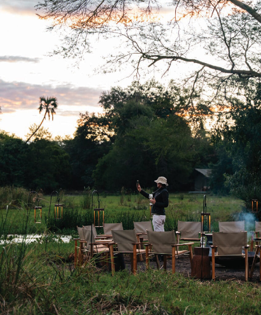Guests gathered around an outdoor dining area overlooking a lush wetland at Mozambique Gorongosa Conservation Safari