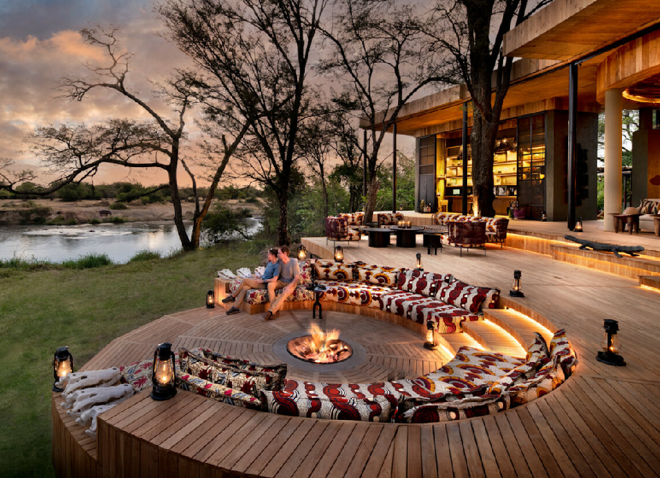 Luxury safari camp riverside deck in Tanzania with a fire pit, outdoor seating, lanterns, and views of the surrounding landscape.