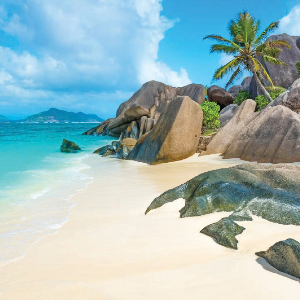 Tropical island lagoon with crystal-clear turquoise water, lush green hills, and a bright blue sky with clouds.