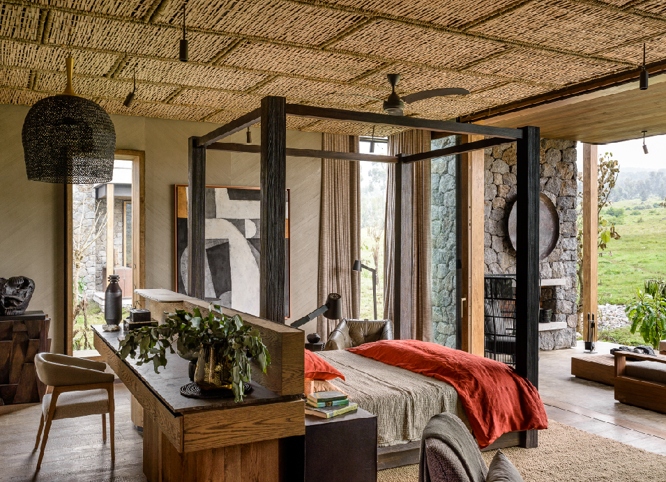 Stylish Kiwitonda House bedroom with a four-poster bed, red throw, stone walls, woven ceiling, and views of the green landscape.