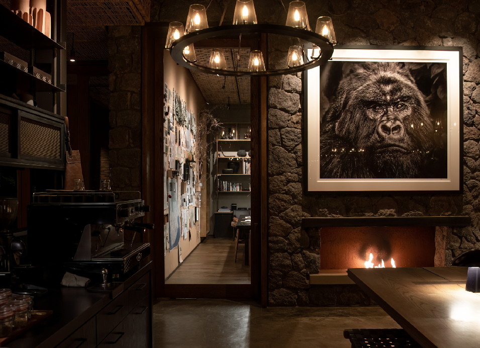 Cozy Kiwitonda Lodge interior with a stone fireplace, framed gorilla portrait, warm lighting, and rustic dining area.