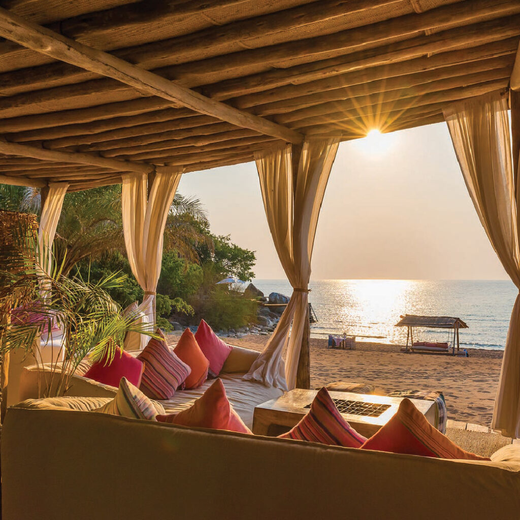 Safari lodge with a shaded canopy, overlooking the ocean and a small boat at sunset in Malawi.