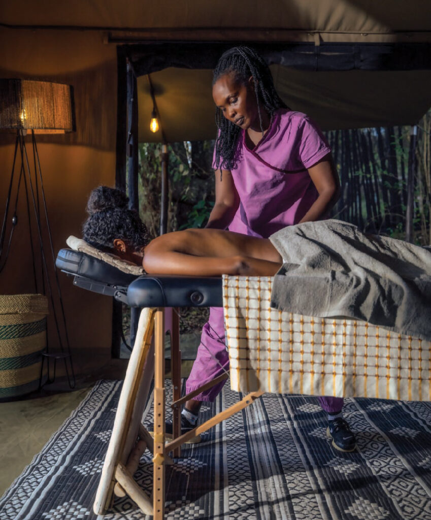 Woman receiving a relaxing massage at a safari lodge, lying on a massage table in a cozy tented spa setting.