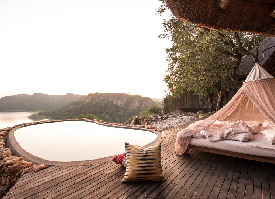 Luxury safari lodge deck with a canopy bed, outdoor plunge pool, and scenic river valley view