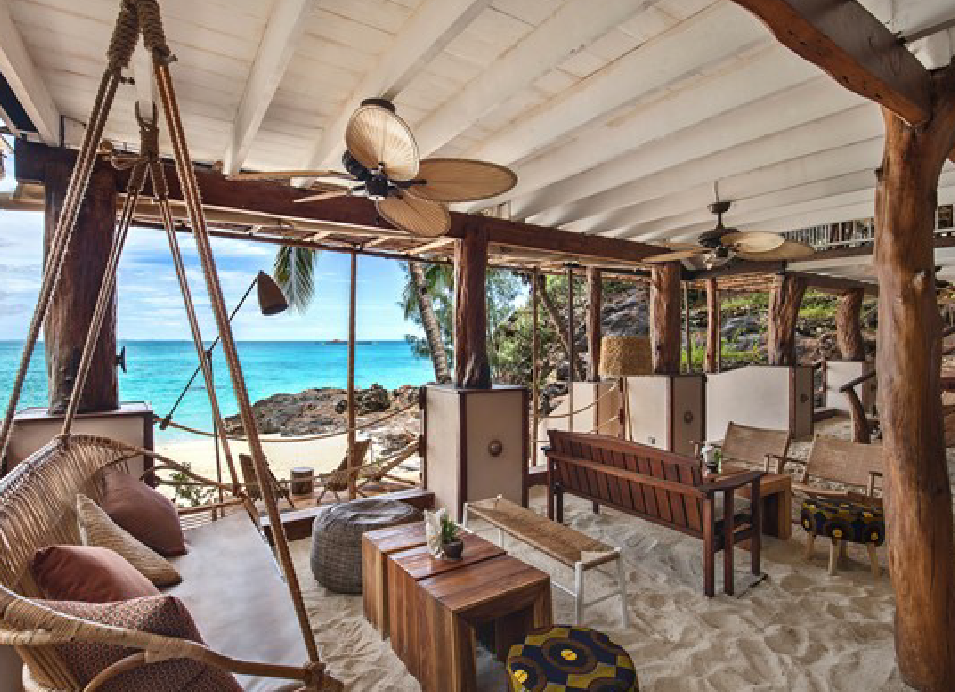 Tropical beachfront lodge with comfortable seating overlooking turquoise ocean water and rocky coastline.