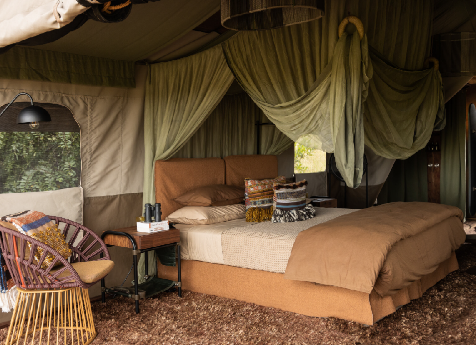 Luxury safari tent bedroom in Tanzania with a king-size bed, draped canvas, cozy seating, and colorful African-inspired cushions.