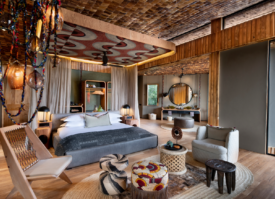 Luxury safari lodge bedroom with a king-size bed, natural wood interiors, woven ceiling, lounge chairs, and African-inspired décor.