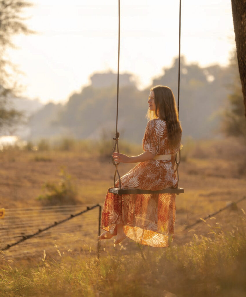 Woman sitting on a swing at sunset in the African wilderness during a safari experience.