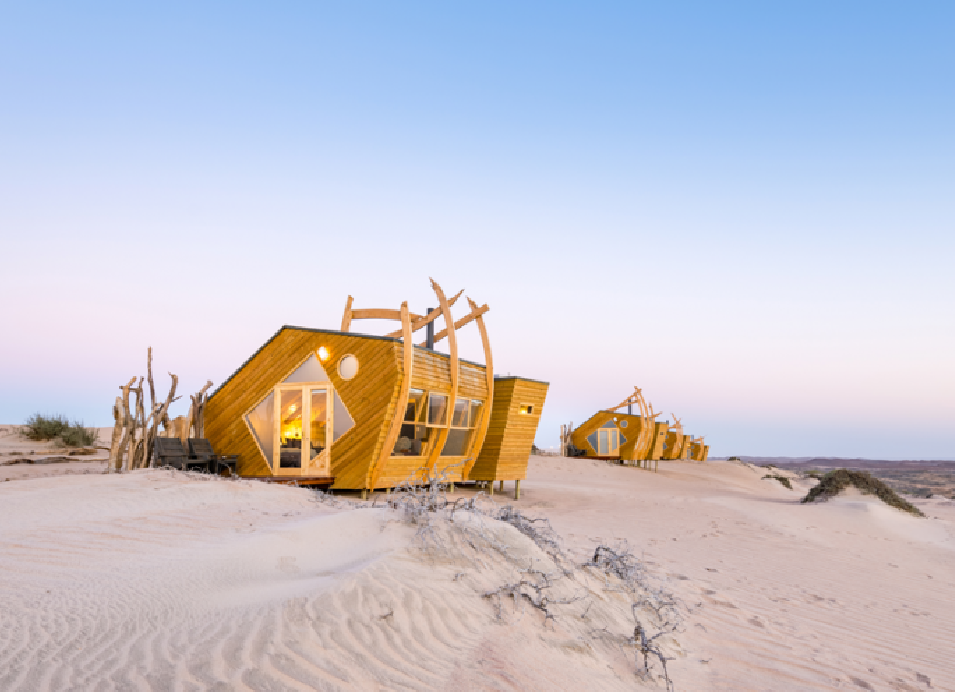 Wooden desert cabins nestled in white sand dunes near the coast of Namibia at sunset.