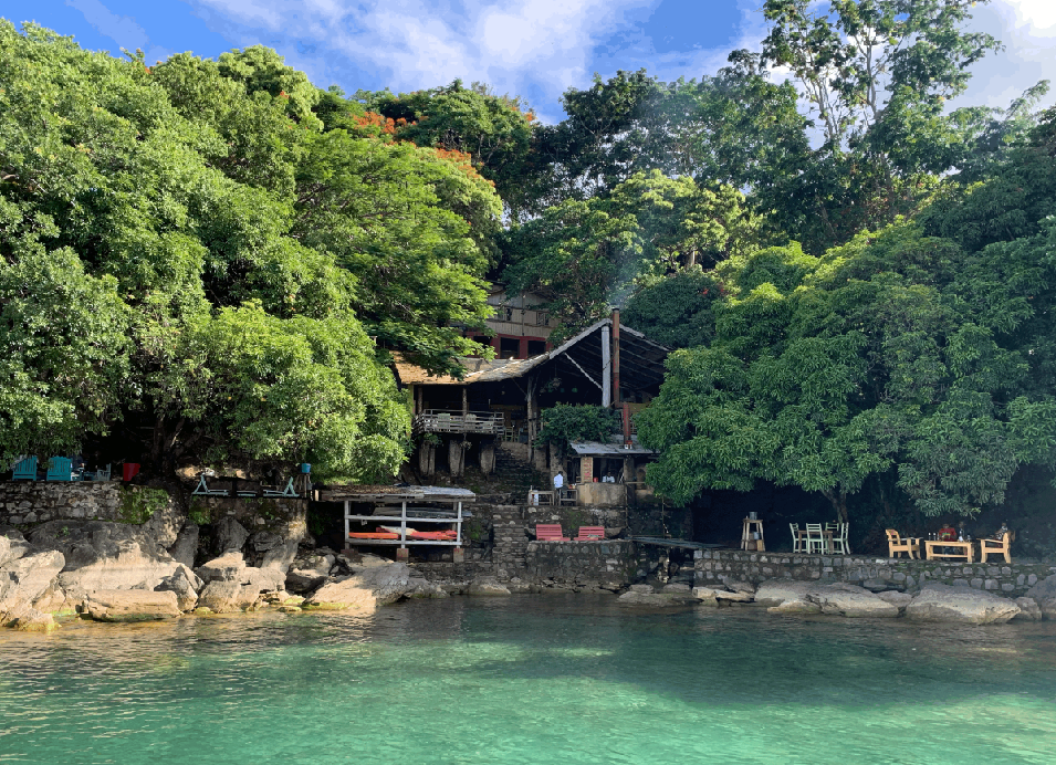 Waterfront restaurant surrounded by lush tropical greenery and turquoise water